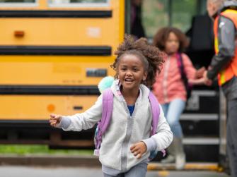 Smiling girl comes off the school bus.